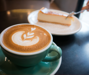 Tasse Kaffee, im Hintergrund ein Stück Kuchen